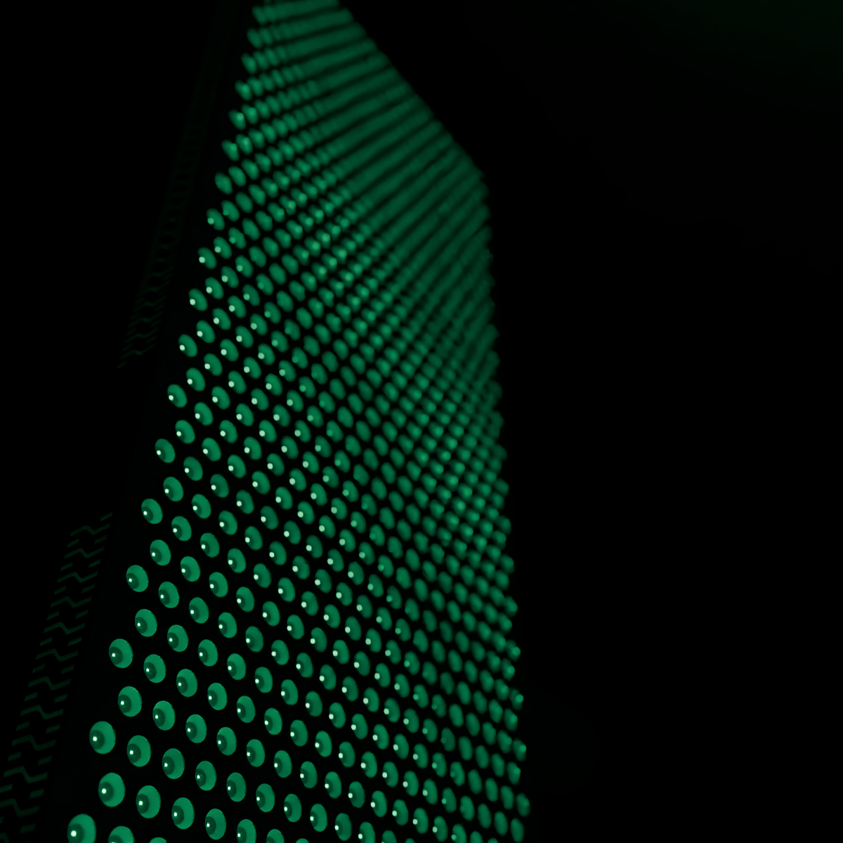 Raking close view along the lit panel face of the DRKD Retreat 189, rows of green LEDs in reflector cups receding into shallow focus.