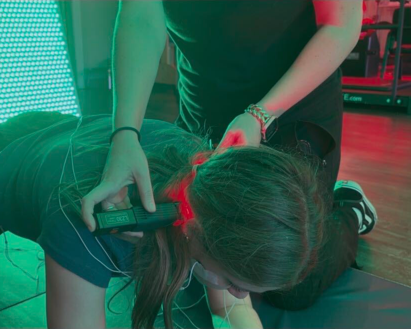 A clinician kneeling beside a person on an exercise mat in a clinic room.